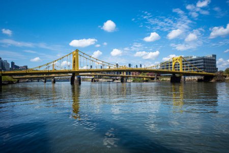 Foto de Un cielo azul con nubes esponjosas sobre el río Allegheny en Pittsburgh, Pensilvania, con el puente amarillo Rachel Carson a la vista. - Imagen libre de derechos