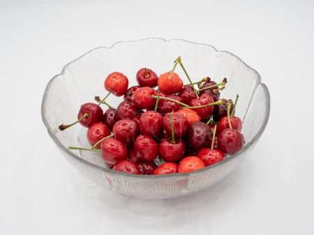 Photo for Organic red cherries, glistening with refreshing water droplets, elegantly presented in a pristine glass bowl, perfectly isolated on a clean white background. - Royalty Free Image