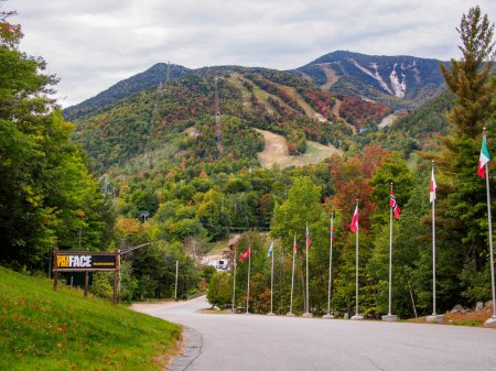 Experience the exhilarating Olympic downhill ski slopes of Whiteface Mountain adorned with vibrant flags, as they intertwine harmoniously with the enchanting fall scenery of Lake Placid in upstate New York.
