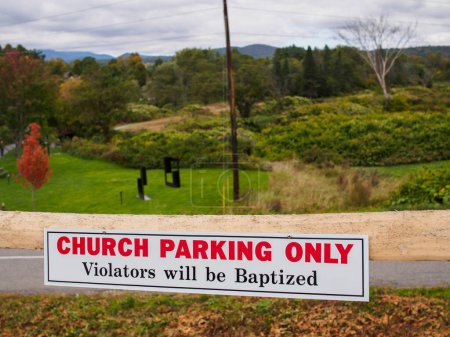 Foto de Cartel divertido fuera de una iglesia en Stowe, Vermont, EE.UU., con montañas en el fondo "Solo los infractores de estacionamiento de la iglesia serán bautizados" - Imagen libre de derechos