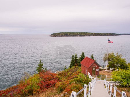 Photo for From Owl's Head Lighthouse in Maine, USA, behold a captivating view of the sea adorned with vibrant fall foliage, while an American flag gracefully waves in the breeze. - Royalty Free Image