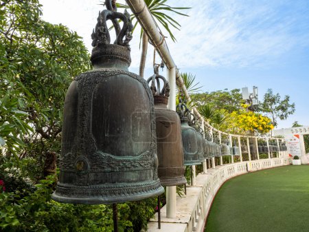Foto de Las campanas de bronce forman una curva elegante en medio de árboles verdes y un cielo azul vivo en el Wat Saket de Bangkok, el Monte Dorado. - Imagen libre de derechos