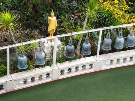 Photo for Viewed from above, a row of bells stretches before a golden Buddha statue, set against a backdrop of lush greenery at Bangkok's Wat Saket, the Golden Mount. - Royalty Free Image