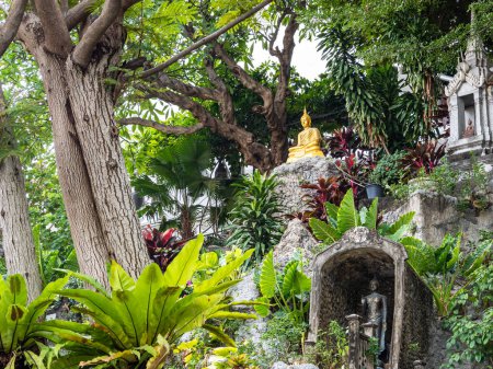 Photo for A serene garden featuring palm trees and a seated golden Buddha statue on a temple cliff at Bangkok's Wat Saket, the Golden Mount in Thailand. - Royalty Free Image