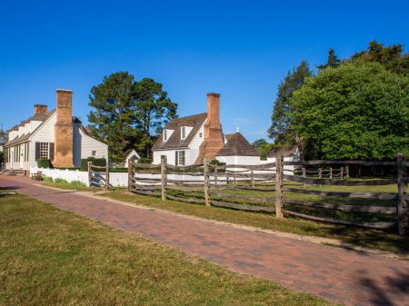 Photo for Vintage white houses, adorned with brick chimneys, bordered by a serene walkway and wooden fence, all beneath a clear blue sky in Williamsburg, Virginia. - Royalty Free Image