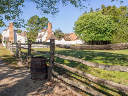 Photo for A wooden fence and barrel leading to white colonial houses beneath a clear blue sky in Williamsburg, Virginia. - Royalty Free Image