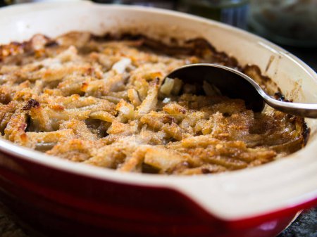 Photo for Traditional Swedish delicacy, Jansson's Frestelse: a casserole of potatoes, onions, anchovies, and rich cream, often enjoyed during Christmas, presented in a red pan with a serving spoon. - Royalty Free Image