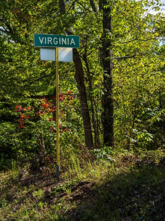 Photo for A road sign of Virginia indicating the border with West Virginia, set against a backdrop of lush forest scenery. - Royalty Free Image