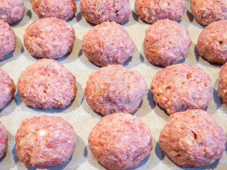 Photo for Delectable meatballs, neatly arranged on a baking tray lined with parchment paper, poised for their initial oven bake preceding the frying process. - Royalty Free Image