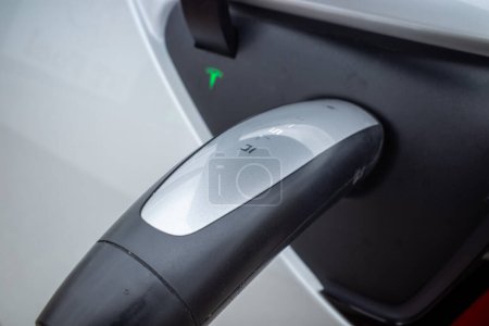Photo for The new era of transportation. A closeup view of the handle of an electric charger securely plugged into a Tesla. - Royalty Free Image
