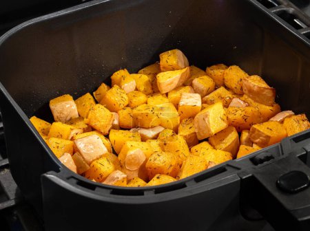 Photo for Detailed close-up showcases healthful cubes of butternut squash in an air fryer, enhanced with aromatic herbs for a nutritious and flavorful culinary delight. - Royalty Free Image
