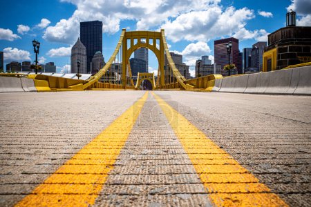The Rachel Carson Bridge spans Allegheny River gracefully with road markings, its vibrant yellow hue contrasting against the backdrop of downtown Pittsburgh.