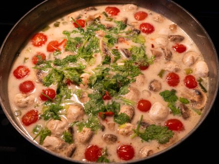 Diese köstliche asiatische Suppe mit Kokosmilch, Champignons, Huhn, Kirschtomaten und Koriander ist ein köstlicher Geschmack Südostasiens. Hier serviert in einer Metallschüssel.