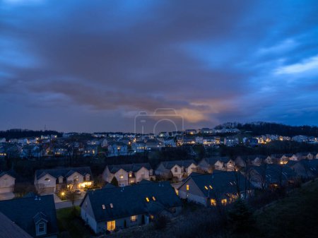 Photo for Aerial view: Dramatic clouds and glowing windows illuminate a US neighborhood at dusk. - Royalty Free Image