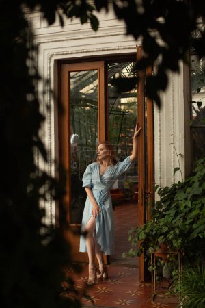 Téléchargez les photos : Jeune femme en robe bleue posant dans un jardin botanique tropical avec de la verdure sur le fond - en image libre de droit
