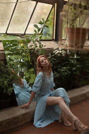 Foto de Mujer joven en vestido azul posando en jardín botánico tropical con vegetación en el fondo - Imagen libre de derechos