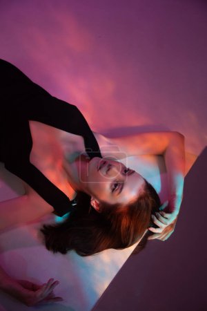 Foto de Retrato de mujer joven en vestido negro con reflejo de luz de neón en el cuerpo sobre fondo multicolor - Imagen libre de derechos