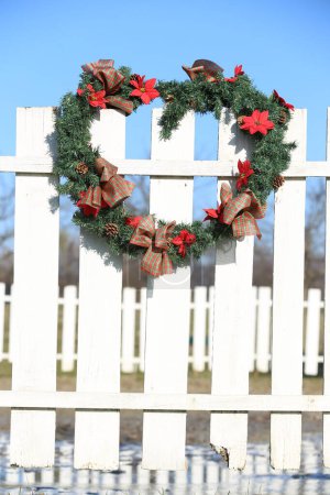 Hermosa corona de Navidad colgando de la valla de corral en la granja rural de animales navideños. Maravillosa decoración de Navidad hecha a mano 