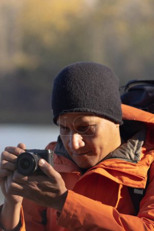 Téléchargez les photos : Portrait de voyageur homme au lac en automne prendre une photo avec l'appareil photo numérique. Photo de haute qualité - en image libre de droit