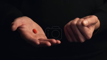 Studio shot mains masculines montrent pilule rouge isolé sur fond noir. Concept de faire le bon choix.