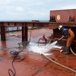 at sea - october 16, 2023 : ship's crew hosing down at cross deck of a cape size bulk carrier for deck cleaning purpose