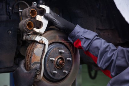 mechanic at a car service diagnoses and replaces the caliper and brake pads in the front of the car. Car without wheels. metal spare parts. holds the brake disc with both hands