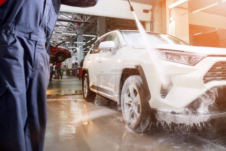 Mann wäscht weißes Auto mit Druck mit Wasser Platz, um das Auto beim Autoservice zu reinigen. Shampoo und Wasser.