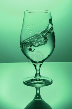 splash in a glass goblet with water on a colored in green background