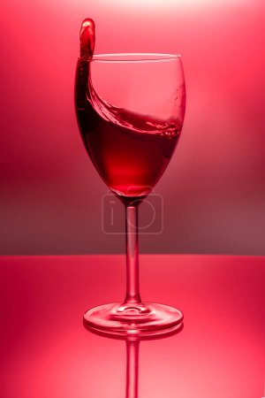 splash in a glass goblet with red wine on a colored in red background