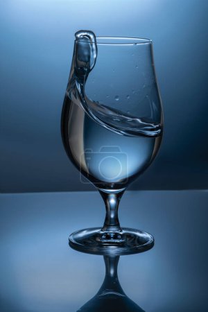splash of a transparent liquid in a glass goblet with water or gin on a colored in blue background