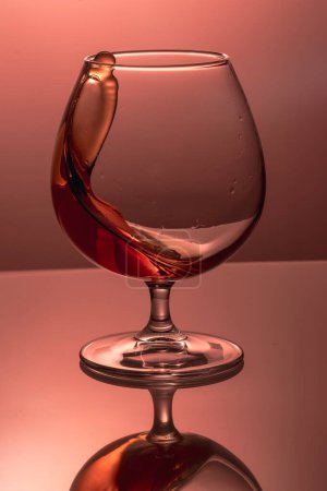 splash in a glass goblet with a cognac on a colored in pink background
