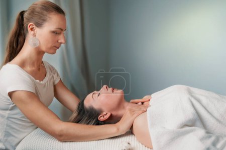 A woman is receiving a soothing massage at a spa, feeling comfort as skilled hands work on her muscles, relaxing her neck, jaw, and eyelashes with gentle gestures
