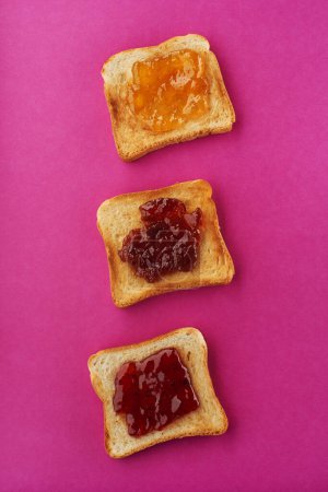 Photo for Three crispy slices of toast with strawberry, apricot and fig jam on bright pink background - Royalty Free Image