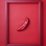 Whole red pepper in wooden picture frame on red background