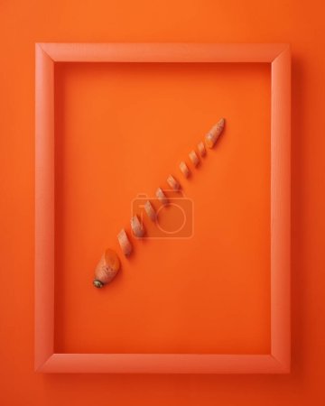 Photo for Chopped carrot in wooden picture frame on orange background - Royalty Free Image