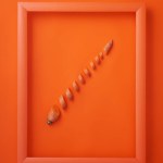 Chopped carrot in wooden picture frame on orange background