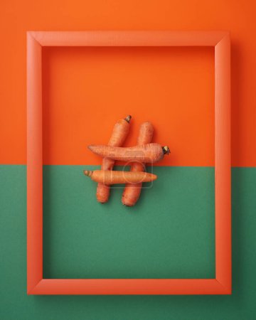 Hashtag symbol from carrots in wooden picture frame on orange and green background