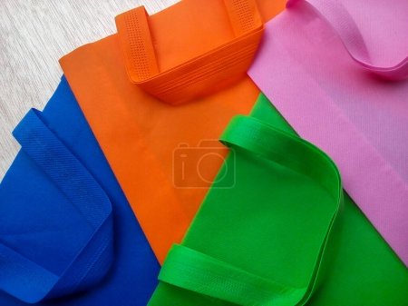 Foto de Bolsas de polipropileno rosa, verde, naranja y azul. una pila de bolsas hechas de tela no tejida con pliegues en un tablero fibroso blanco - Imagen libre de derechos