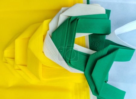 Foto de Bolsas no tejidas verdes, amarillas y blancas. un conjunto de bolsas de polipropileno poroso apiladas y plegadas - Imagen libre de derechos