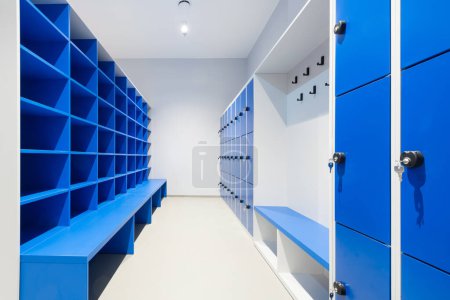 Téléchargez les photos : Casiers bleus sur un mur avec clé dans une serrure et armoire avec étagères vides et banc - en image libre de droit