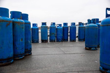 array of used blue propane gas cylinders lined up on concrete floor, essential supplies for industrial welding and heating tasks