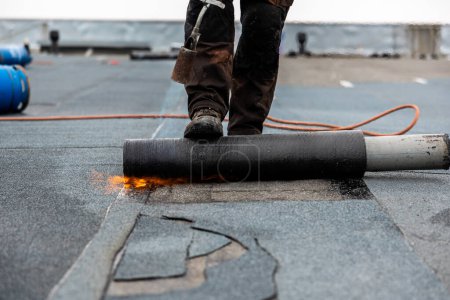 professionelle Dachdecker bei der Arbeit Sicherung von gerolltem Teerpapier mit einer Lötlampe auf einem Flachdach Installationsprozess
