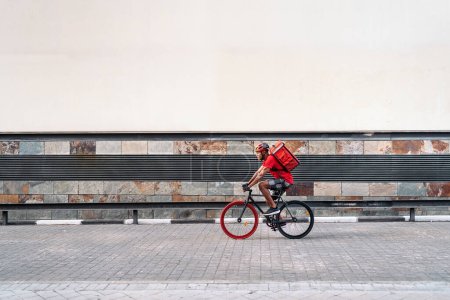 Foto de Repartidor africano llevando un paquete y usando un casco de seguridad cruzando la ciudad con su bicicleta. - Imagen libre de derechos