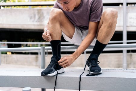 Photo for Cool young man tying his sneakers laces before doing parkour tricks in the city. - Royalty Free Image