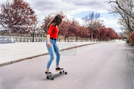 Téléchargez les photos : Femme patineuse cool pratiquant avec son longboard dans le parc et s'amusant. - en image libre de droit