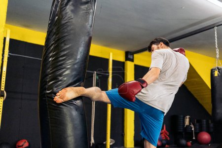 Foto de Luchador de Kickboxing realizando patadas con pie en el saco de boxeo en el gimnasio. Concepto de kickboxing. - Imagen libre de derechos