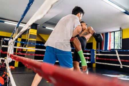 Téléchargez les photos : Deux jeunes hommes adultes s'entraînent à donner des coups de pied contre des mitaines que l'un d'eux tient sur le ring. Concept de kickboxing. - en image libre de droit