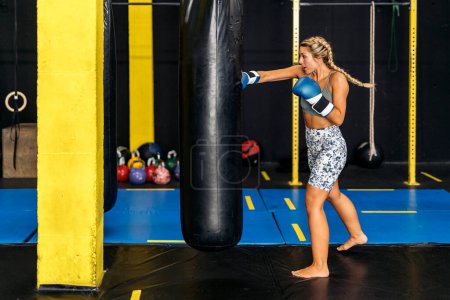 Foto de Mujer adulta joven caucásica golpeando un saco de boxeo en el gimnasio. Concepto de caja y formación. - Imagen libre de derechos