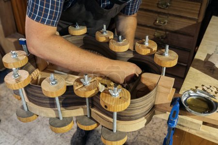 Téléchargez les photos : Un artisan méconnu crée une guitare et utilise des outils dans un atelier traditionnel. - en image libre de droit