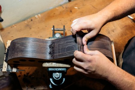 Photo for Unrecognized luthier sanding a guitar in his workshop and using tools. - Royalty Free Image